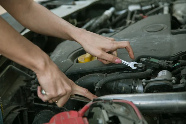 Mano femenina con una llave inglesa bajo el capó del coche — Foto de Stock