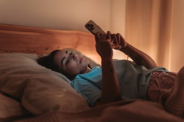 Uzaktan kumandalı kadın çalışan telefondaki e-postayı kontrol ediyor. Sıcak lamba ve sıcak battaniye, odaklanmış yüz ve geç saatte...