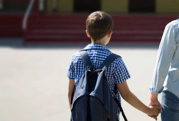 Ebeveyn ve öğrenci el ele gidiyor. Sırt çantalı kadın ve çocuk..