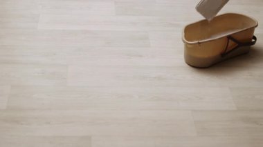 Bir paspas, yakınlarda bir kova ile hafif ahşap bir zemin temizliyor..