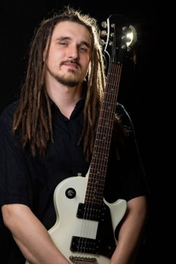 Elinde elektro gitar tutan, gözleri kapalı, gülümseyen, siyah bir arka plana bakan uzun saçlı bir adam.