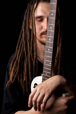 Elinde elektro gitar tutan, gözleri kapalı, gülümseyen, siyah bir arka plana bakan uzun saçlı bir adam.