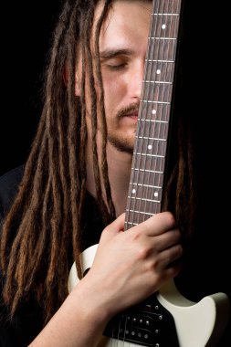Elinde elektro gitar tutan, gözleri kapalı, gülümseyen, siyah bir arka plana bakan uzun saçlı bir adam.