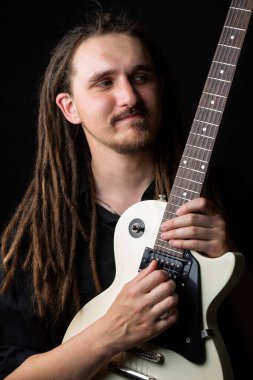 Elinde elektro gitar tutan, gözleri kapalı, gülümseyen, siyah bir arka plana bakan uzun saçlı bir adam.