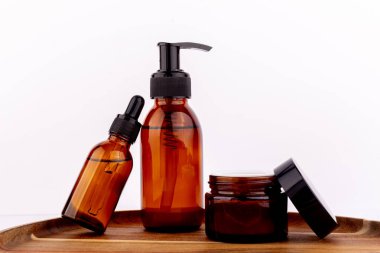 Kehribar cam şişeler ve kavanoz ahşap bir tepsi üzerinde beyaz bir arka plan karşı.