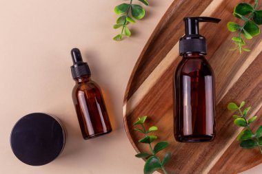 Kehribar kozmetik şişeleri ve okaliptüs yapraklı kavanoz bej arka planda doğal bir güzellik düzlüğü oluşturur.