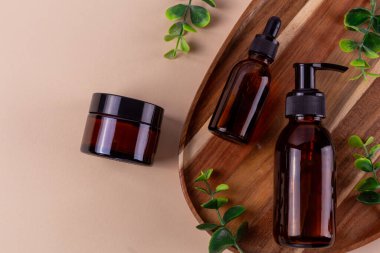 Serum, krem ve losyon için kehribar kozmetik kapları, bej arka planda okaliptüs yaprakları