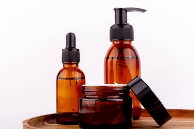 Üç kehribar cam kap, bir damlatıcı şişe, bir pompa şişesi ve bir açık kavanoz dahil, ahşap bir tepside beyaz bir arka plana karşı düzenlenir.