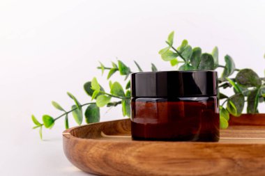 Küçük kehribar bir kavanoz taze yeşil okaliptüs dallarının yanındaki ahşap tepside duruyor.