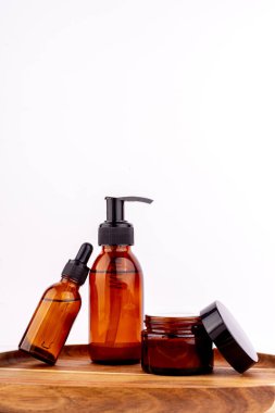 Bir damla şişesi, bir pompa şişesi ve küçük bir kavanoz da dahil olmak üzere kehribar cam kaplardan oluşan bir kolleksiyon, temiz beyaz arka plana karşı kırsal ahşap bir yüzeye yerleştirilmiş.