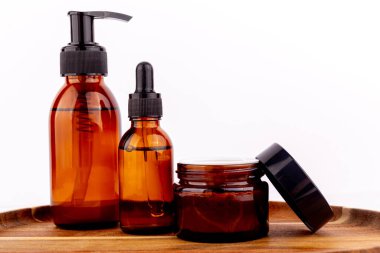 Bir pompa şişesi, bir damla şişesi ve bir kavanoz da dahil olmak üzere üç kehribar cam kap ahşap bir tepside kozmetik formülasyonlar için hazırlandı.