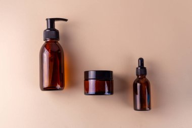 Bir pompa şişesi, bir kavanoz ve bir damlatıcı şişesi de dahil olmak üzere üç kehribar cam kap bej rengi bir yüzeye yerleştirilmiştir.