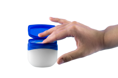 Bir insanın eli açık bir kavanoz petrolden yapılmış jöleye uzanır ve deriye uygulanması için küçük bir miktar alır.