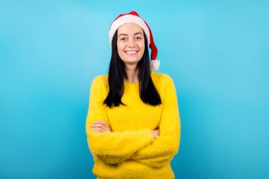 Gülen güzel bayanın, kış tatillerini boş uzay aile partilerini kutlarken çekilmiş fotoğrafı. Noel Baba şapkası, sarı kabarık süveter, izole edilmiş mavi arka plan. Çekici sırların portresi