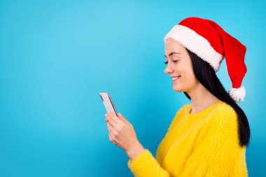 Profil tarafı fotoğrafı oldukça komik bayan kol tutuşu modern telefon aygıtı kullanın Noel Baba şapkası standı boş alan mavi renk arka grubunda izole