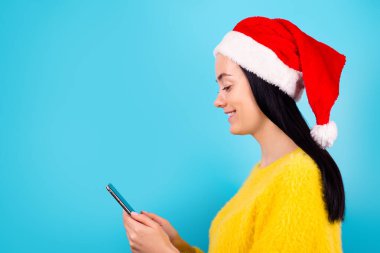 Profil tarafı fotoğrafı oldukça komik bayan kol tutuşu modern telefon aygıtı kullanın Noel Baba şapkası standı boş alan mavi renk arka grubunda izole