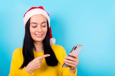 Heyecanlı komik bayanın fotoğrafı. Noel Baba şapkası, telefonun mavi renk arka grubunda izole olduğunu gösteriyor.