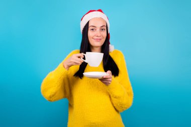 Neşeli bayanın fotoğrafı beyaz kahve aromalı, aromalı, kokulu sarı süveterli, izole mavi arka grup elbisesi giyiyor.