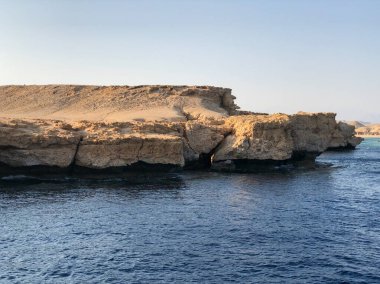 Engebeli, güneşten sırılsıklam olmuş bir yamaç yüzeyi derin mavi denizle buluşur ve kıyı manzarasının ham güzelliğini gözler önüne serer.