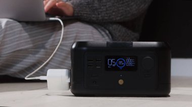 Bir kişi taşınabilir güç istasyonuna bağlı bir dizüstü bilgisayar kullanıyor, bu da uzaktan çalışma için elektrik şebekesi veya yedek güç çözümlerini gösteriyor