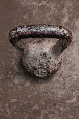 Yıpranmış boya ve pas da dahil olmak üzere aşınma ve yırtık belirtilerini gösteren eski bir kettlebell desenli beton bir yüzeye oturur.