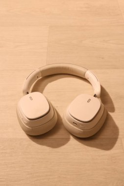 Bir çift modern beyaz kulaklık temiz, açık renkli ahşap bir yüzeye yerleştirilmiş, onların minimalist estetik ve ses teknolojilerini vurguluyor.