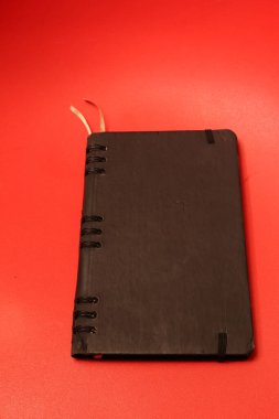 Siyah elastik bir kapağı olan koyu deri kaplı bir günlük ve parlak kırmızı bir yüzeye bağlı ince bir kurdele yer imi.