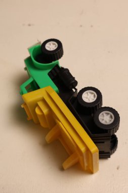 İki oyuncak kamyonun yakın plan görüntüsü, biri yeşil diğeri sarı, siyah tekerlekler ve detaylar, tarafsız bir arkaplanda dinleniyor.