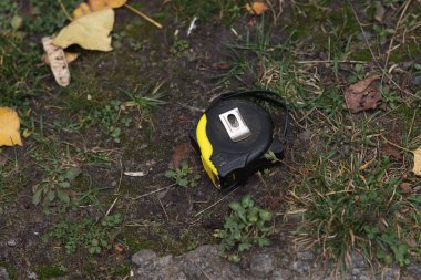 Bu yakın çekim, yeşil çimenler ve sonbahar yapraklarıyla çevrili, toprakta atılmış bir mezura ölçer. Bu da unutulmuş bir aleti işaret eder.