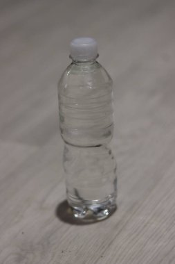 Tek, boş, berrak, beyaz kapaklı plastik bir su şişesi açık renkli ahşap bir zeminde oturur, ince bir gölge bırakır.