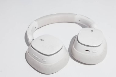 Bir çift parlak, beyaz kulaklık beyaz bir yüzey üzerinde duruyor, çağdaş tasarımlarını ve ince logo detaylarını gösteriyor.