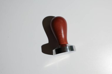 Cilalanmış ahşap saplı ve parlak metal temeli olan bir kahve makinesinin yakın plan çekimi, temiz beyaz arka planda belirgin bir gölge bırakıyor.