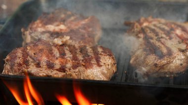 Yakından bakınca, dökme demir ızgara tavasında pişen bifteklerin ızgara izlerinin ve yükselen buharın görüntüsü.