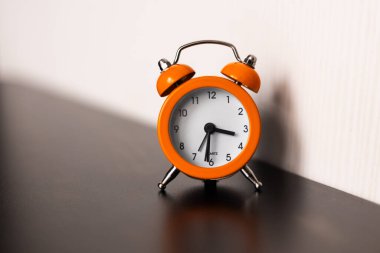 Parlak turuncu kaplamalı, üstünde ikiz ziller olan klasik bir analog çalar saat pürüzsüz, karanlık bir yüzeye ince bir gölge bırakıyor.