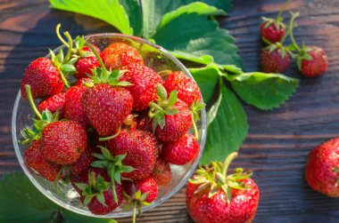 Cam vazoda olgun çilekler var. Tahta masadaki organik meyveler.