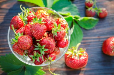 Cam vazoda olgun çilekler var. Tahta masadaki organik meyveler.