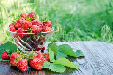 Cam vazoda olgun çilekler var. Tahta masadaki organik meyveler.