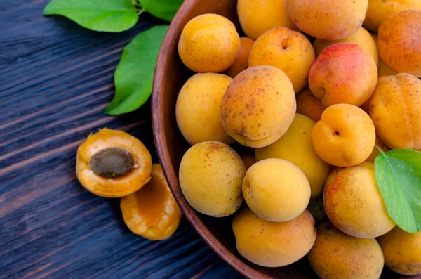 Tahta bir masada yaprakları olan taze, olgun organik kayısılar.