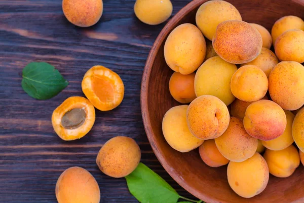 Tahta bir masada yaprakları olan taze, olgun organik kayısılar.