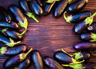 Masanın etrafında kavrulmuş olgun mor patlıcanlar. Masanın içinde boş yer var.