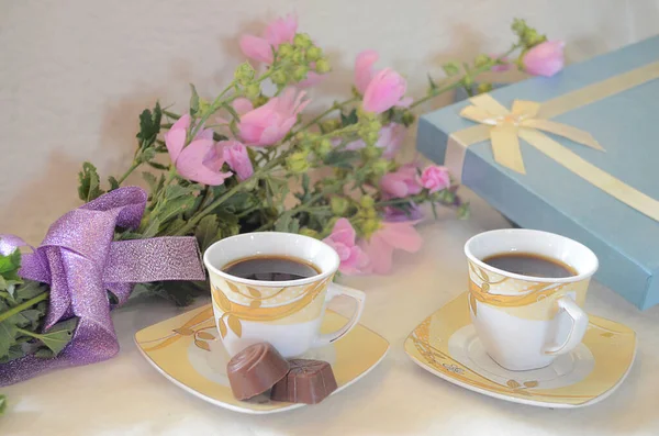 Coffee in a cup, sweets, flowers and a gift box on the table