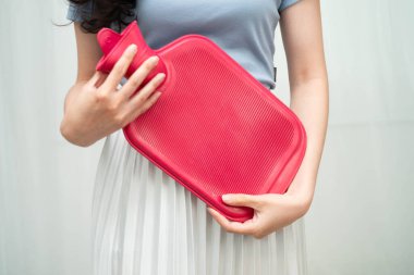 Karın ağrısını hafifletmek için sıcak su torbası kullanan bir kadın..