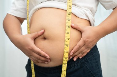 Asyalı kadın şişman göbeğini sıkmak için elini kullanıyor. Büyük boy aşırı kilolu ve obez..