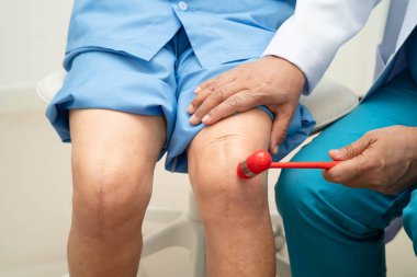 Asyalı doktor, hastanedeki yaşlı hastayı muayene etmek için diz refleksi sinirine vurdu..