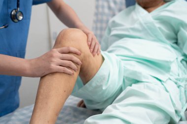 Doktor, hastanede dizinde yara izi olan Asyalı yaşlı kadın hastayı kontrol ediyor..