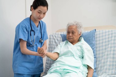 Asyalı doktor yaşlı kadın hasta sağlığını hastanede kontrol edip tedavi ediyor.