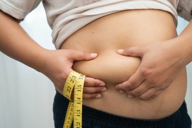 Asyalı kadın şişman göbeğini sıkmak için elini kullanıyor. Büyük boy aşırı kilolu ve obez..