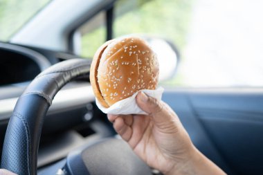Asyalı kadın sürücü arabada hamburger yiyip, tutar, tehlikeli ve kaza riskini göze alır..