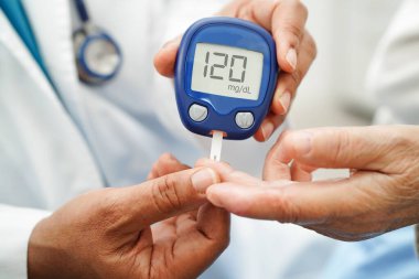 Diyabet tedavisinde kan şekeri seviyesini kontrol etmek için dijital glikoz ölçer kullanan Asyalı doktor.