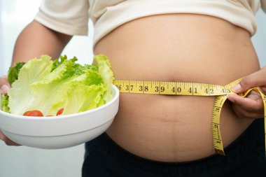 Koca göbekli, şişman, kilolu ve sağlıklı yiyecekleri olan Asyalı bir kadın..